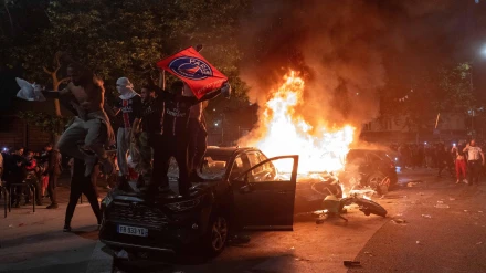 Aficionados del PSG celebran el triunfo de su equipo sobre dos coches en llamas.