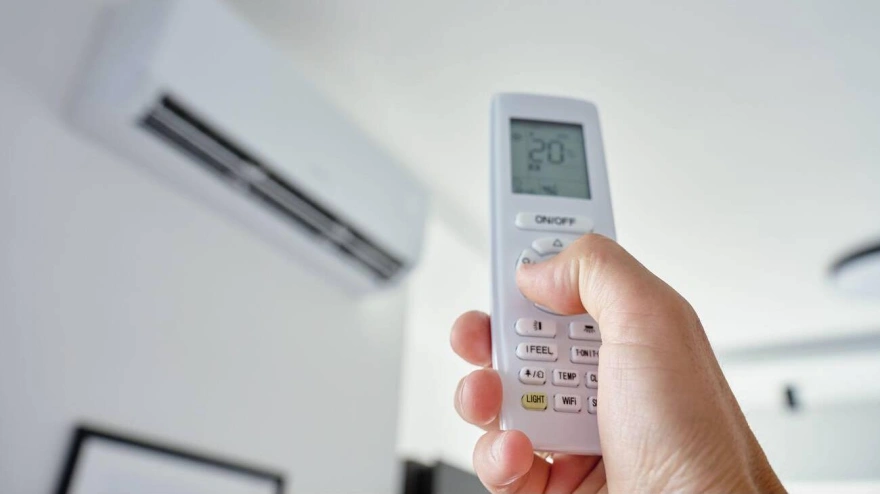 Primer plano de una mano usando el control remoto para ajustar la temperatura de un aire acondicionado