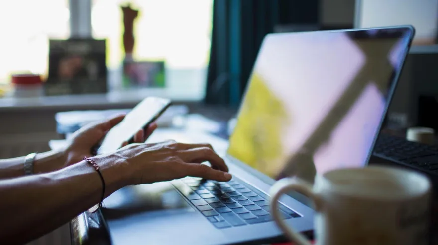 Una mujer teletrabajando desde casa con un ordenador portátil y un teléfono móvil