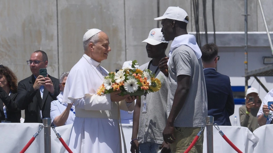El papa León XIV recibe flores de dos voluntarios para protagonizar una ofrenda floral en el mar en recuerdo de los migrantes muertos en la travesía durante el encuentro con más de un millar de inmigrantes de África, América Latina y con representantes de las principales instituciones y organizaciones sociales que trabajan en los servicios de rescate, acogida e integración en el muelle de Arguineguín, en la isla de Gran Canaria