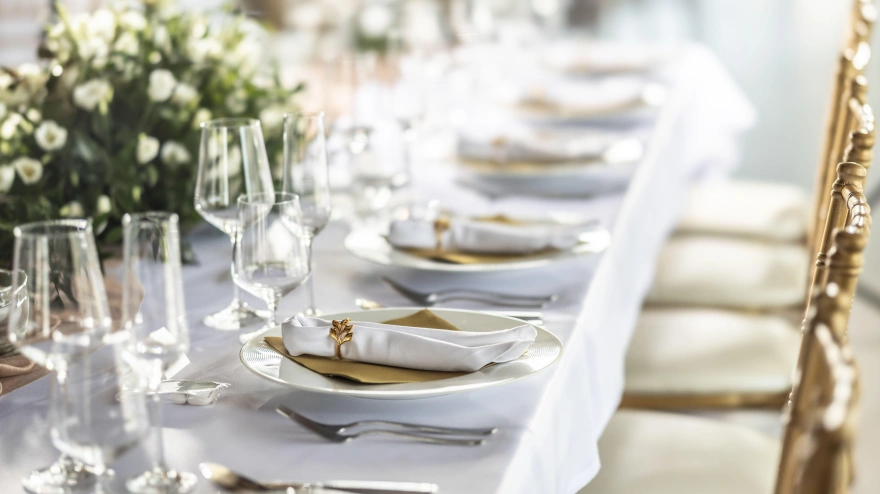 Una mesa de boda cubierta con un mantel blanco, decorada con flores, velas, vasos y cubiertos.