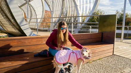 Una joven acaricia a su perro galgo, con un abrigo acolchado rosa, mientras está sentada en un banco en la pasarela de Arganzuela en Madrid.