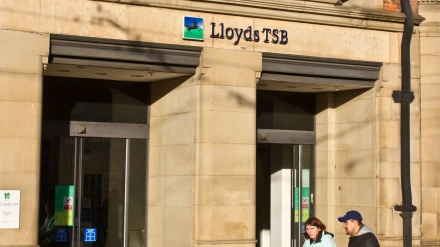 Una pareja joven con un bebé pasa junto a un banco.