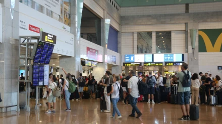 Pasajeros haciendo cola para facturar y consultando las pantallas con información de vuelos en la terminal 2 del aeropuerto del Prat.