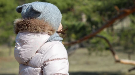 Una niña linda con un sombrero con orejas y una bufanda está de espaldas.