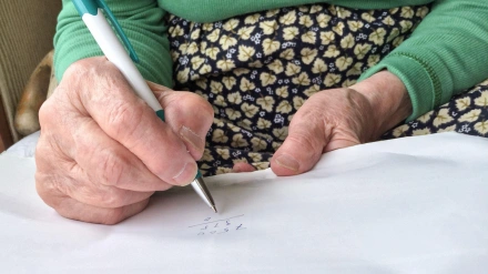 Primer plano de las manos de una mujer mayor firmando un documento