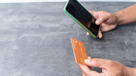 Manos sosteniendo una tarjeta de crédito genérica y un teléfono inteligente