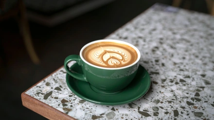 Taza de café Flat White en una taza verde con un hermoso arte latte, sobre una mesa de mármol.