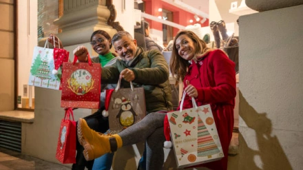 Happy friends showing Christmas shopping bags in front of a store at nigh