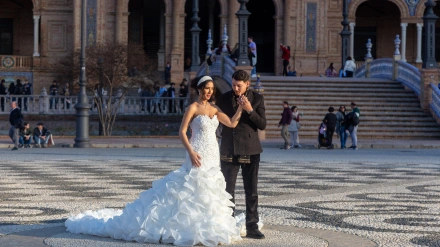 Pareja española enamorada, comprometida. Hermosa novia con vestido blanco largo y traje negro. Plaza de España, Sevilla, Andalucía.