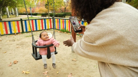 Madre tomando fotografía de niña balanceándose en el patio de recreo