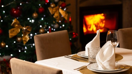 Acogedor comedor navideño con un árbol decorado, una cálida chimenea, luces festivas y una mesa elegante lista para una celebración navideña.
