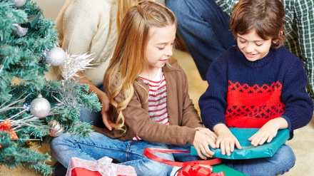 EA0TCW Girl and boy opening christmas gifts together at christmas eve