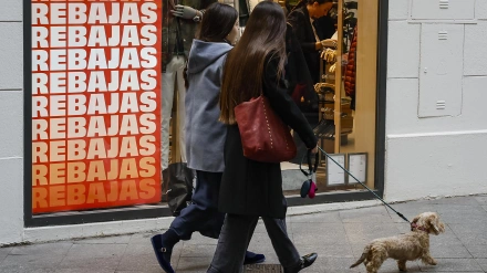 Dos jóvenes paseando por la calle, pasando por una tienda en rebajas