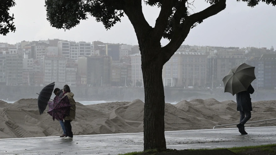Varias personas se protegen de la lluvia junto a la costa de A Coruña