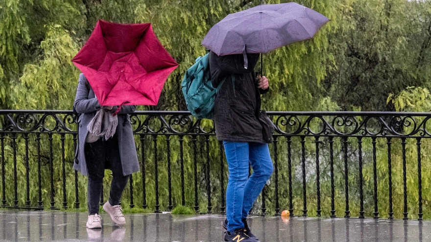 Imagen de archivo de peatones cruzando el puente de Triana en una jornada marcada por la lluvia y el viento.