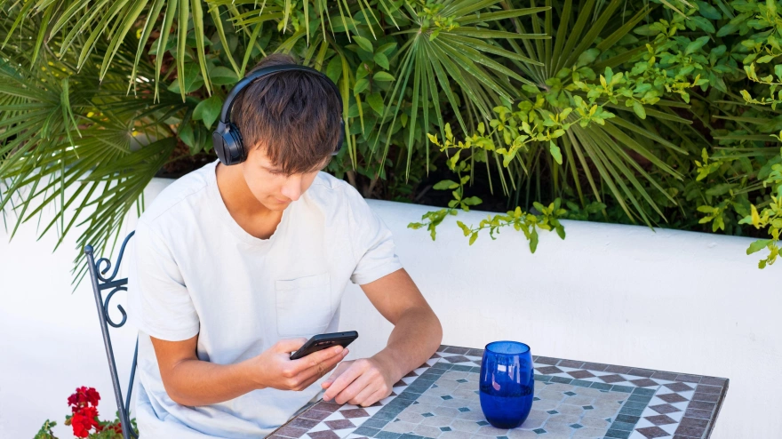 Adolescente sentado al aire libre y mirando el teléfono móvil en sus manos.