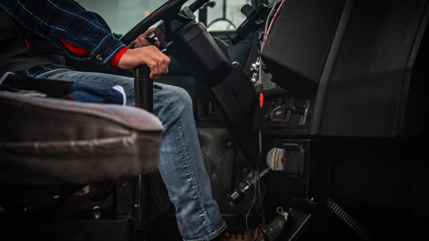 Una persona se sienta en un vehículo, con las manos en el volante, conduciendo activamente y concentrada en la carretera.