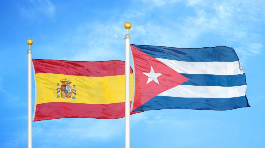 España y Cuba dos banderas en astas y cielo azul nublado