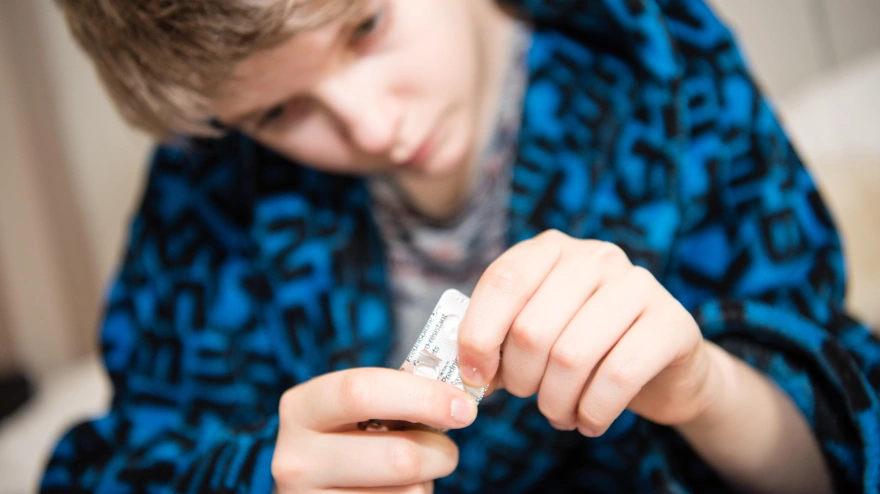 Un adolescente en bata abre un paquete de pastillas de paracetamol