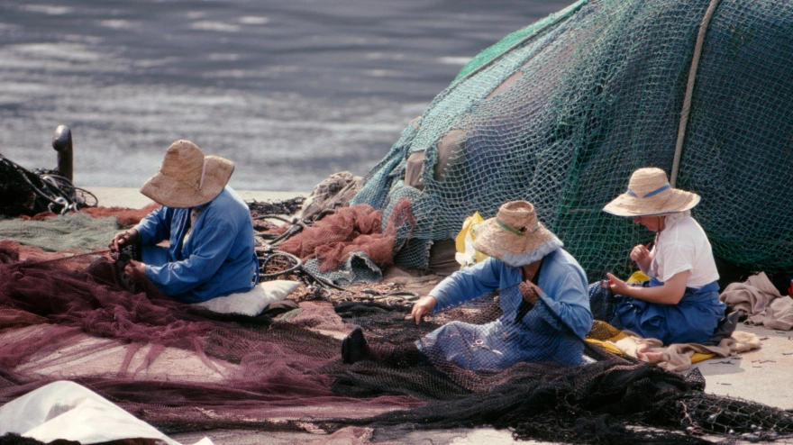 Mujeres remendando redes en el muelle del pequeño puerto pesquero de Caion, provincia de La Coruña, Galicia, España.