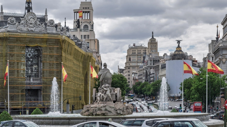 La emblemática fuente de Cibeles y el Banco de España en Madrid, capital de España, rodeados de arquitectura histórica y del tráfico urbano bajo un cielo nublado.